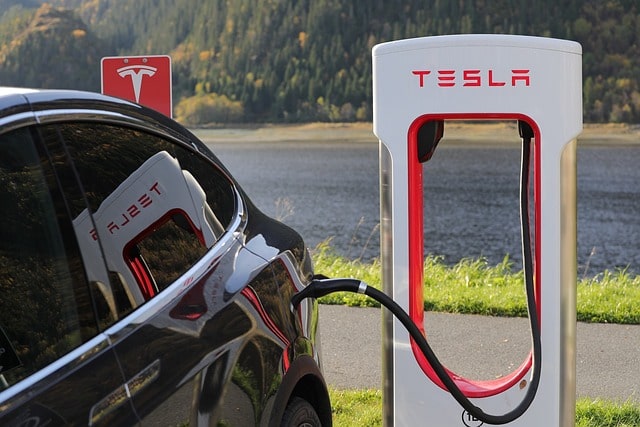 Bild på en elbil av märket Tesla, som står inkopplad till en snabbladdare för att få sitt batteri laddat.